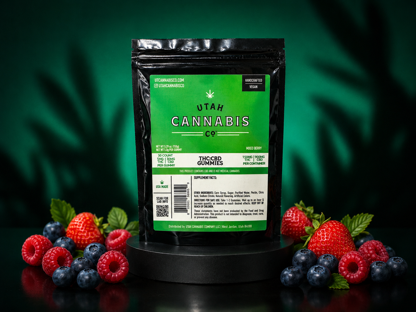 A black stand-up pouch of Utah Cannabis Co. THC-Cannabis Sweets gummies, displayed on a black pedestal with fresh raspberries, blueberries, and green leaves against a dark green background.