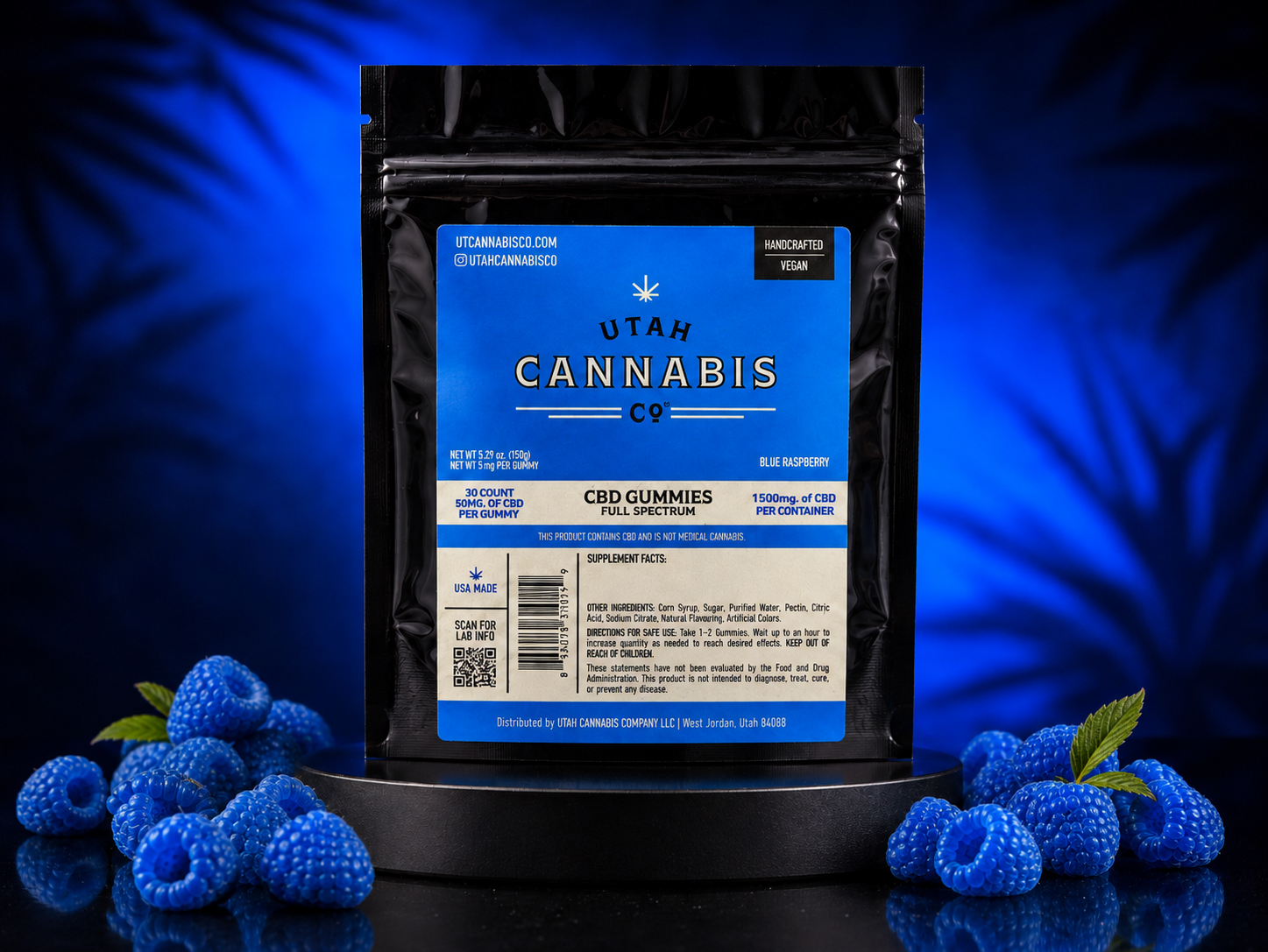 A black stand-up pouch of Utah Cannabis Co. CBD Gummies (Blue Raspberry) displayed on a black pedestal, surrounded by fresh blue raspberries on a reflective dark surface against a dark blue background with leaf shadows.