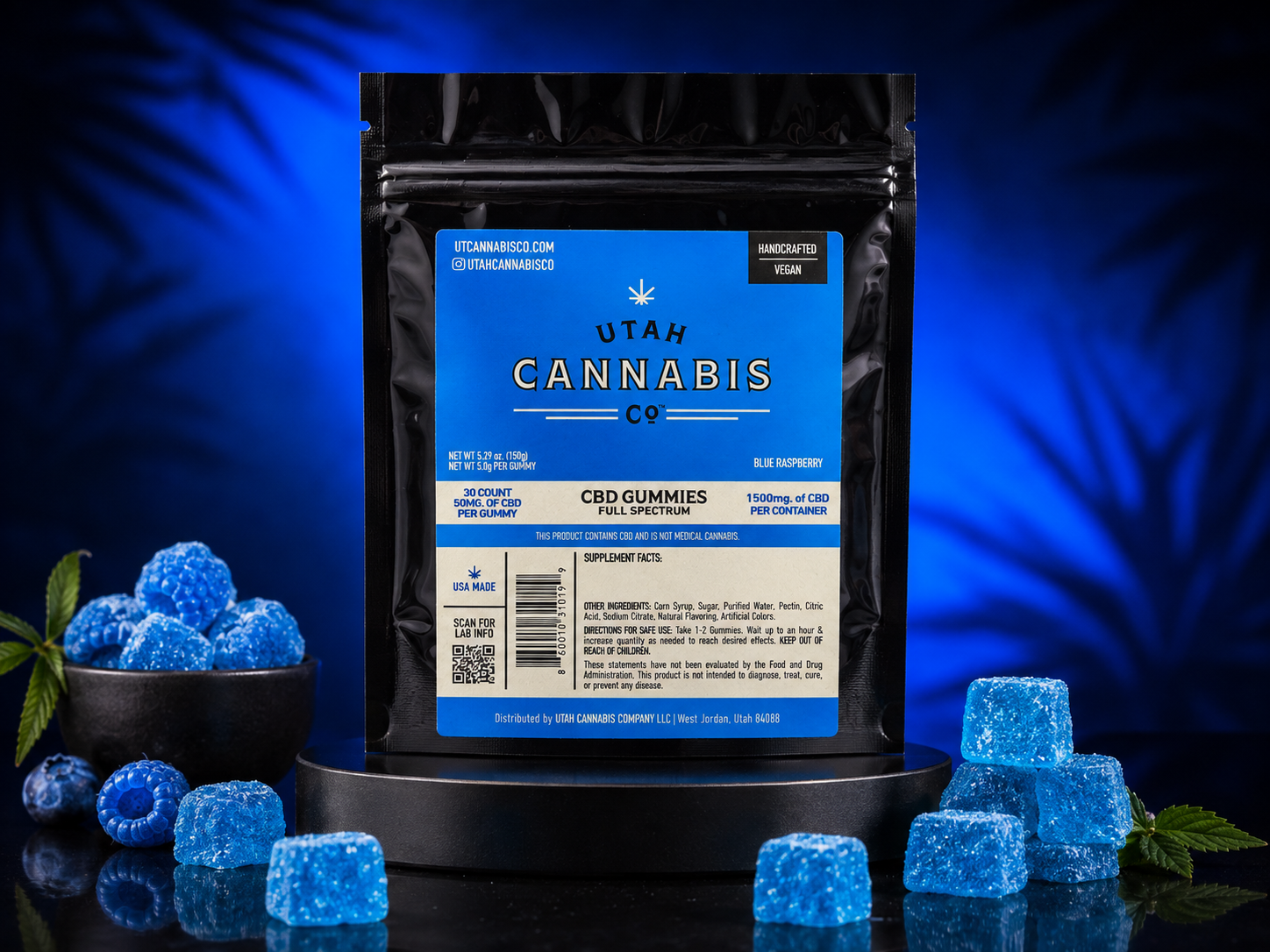 A black stand-up pouch of Utah Cannabis Co. CBD Gummies Blue Raspberry is displayed on a black pedestal against a dark blue background with leaf silhouettes.