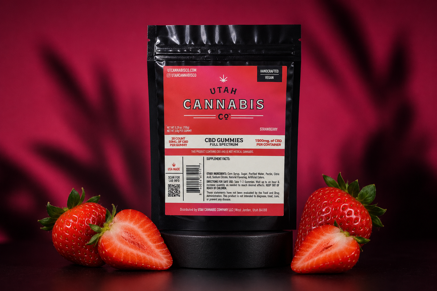 A black stand-up pouch of Utah Cannabis Co. CBD gummies with a red label, displayed on a black surface with fresh whole and sliced strawberries on both sides against a dark red background.